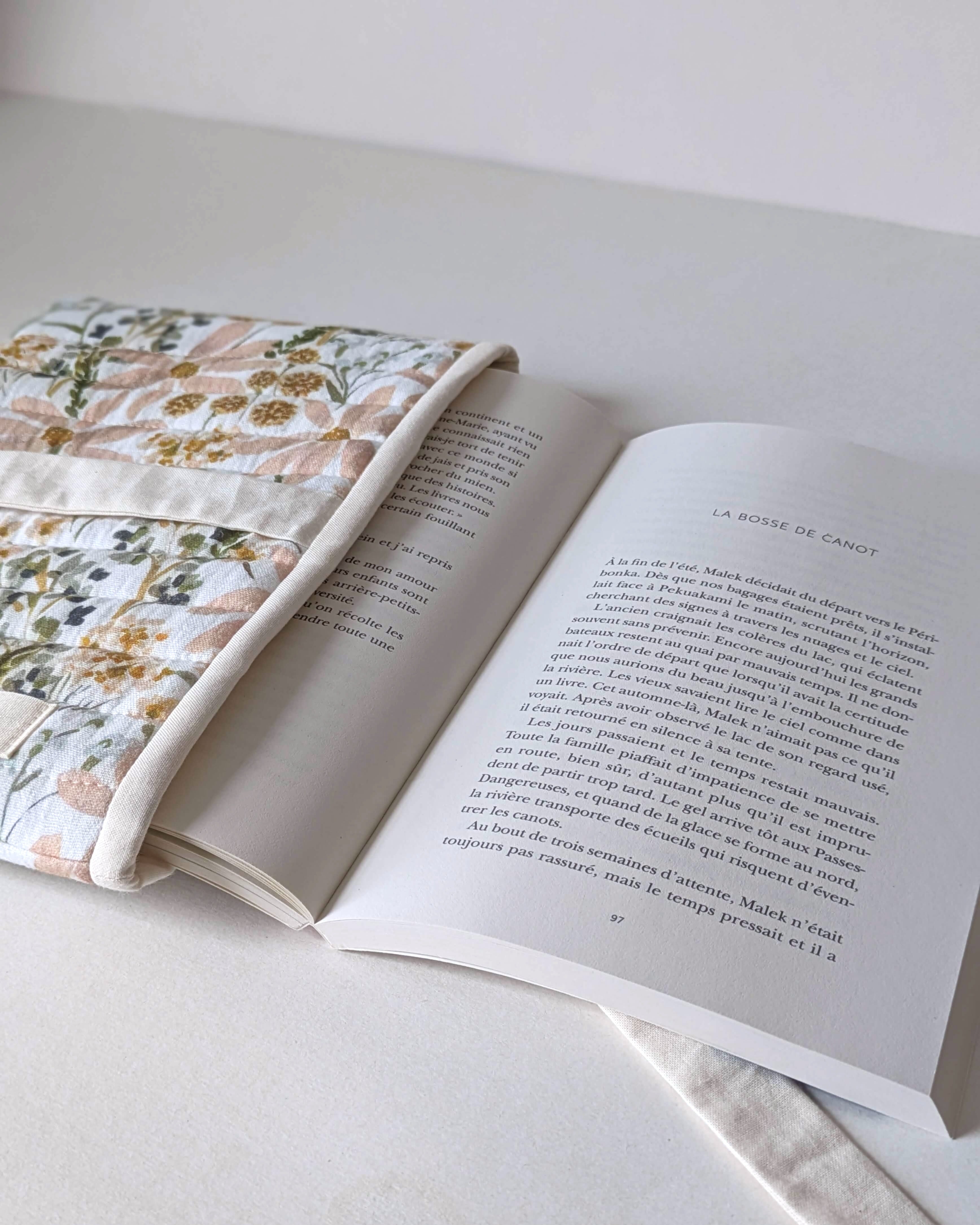 Pochette protège-livre artisanale en tissu fleuri utilisée avec un roman pour protéger les couvertures et les pages.