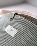 Gros plan sur la tirette en laiton antique et l’étiquette Lou Inspirations d’un sac banane en velours côtelé bio sauge