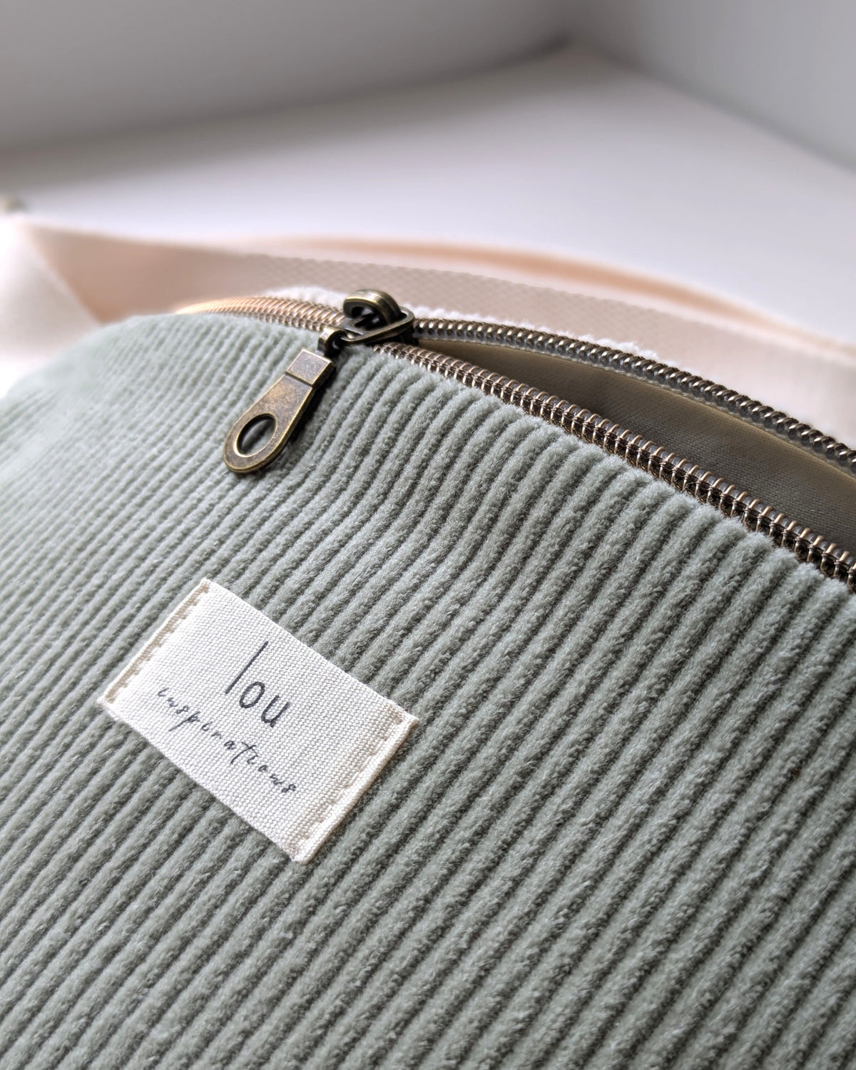 Gros plan sur la tirette en laiton antique et l’étiquette Lou Inspirations d’un sac banane en velours côtelé bio sauge