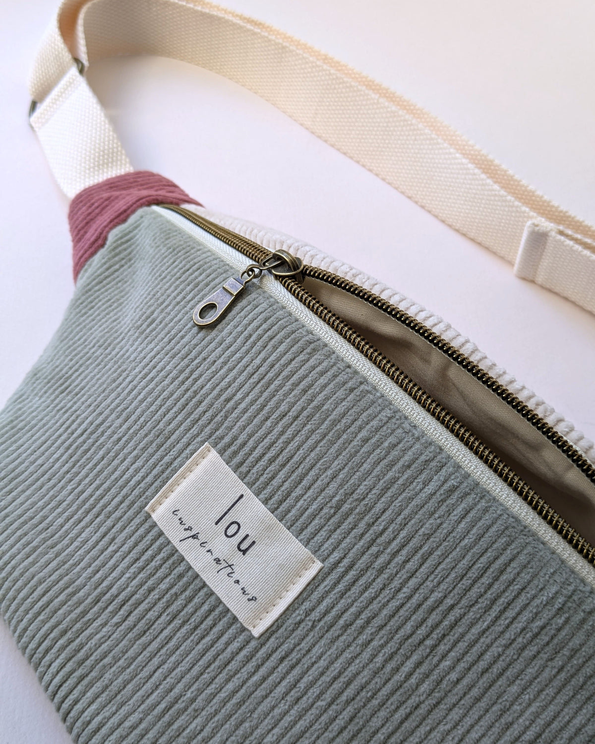 Étiquette Lou Inspirations cousue sur sac banane en velours côtelé vert sauge avec zip bronze et doublure intérieure beige
