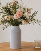 Vase Bota marbre posé sur une table en bois contenant un bouquet de fleurs fraiches. A coté d'une bougie